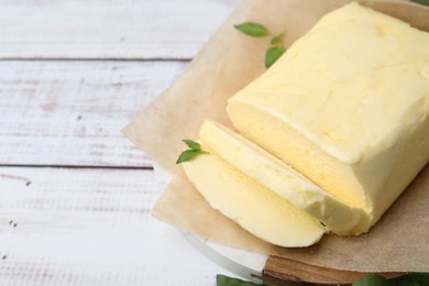 Photo of Cut brick of butter and basil on white wooden table, closeup. Space for text