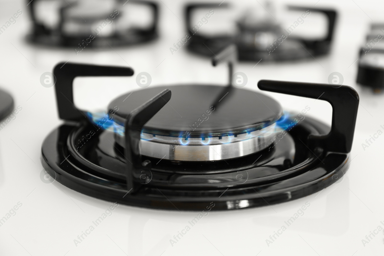 Photo of Gas burner of modern stove with burning blue flame, closeup