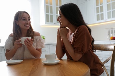 Photo of Young women talking while drinking tea at table in kitchen