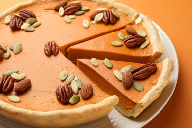 Photo of Tasty homemade pumpkin pie with seeds and nuts on orange background, closeup