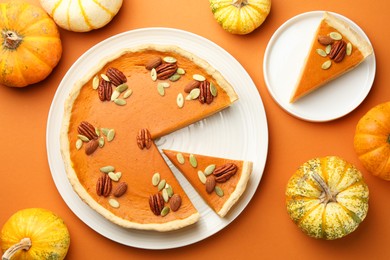 Photo of Tasty homemade pumpkin pie and fresh pumpkins on orange background, top view