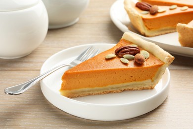 Photo of Piece of tasty homemade pumpkin pie with seeds and nuts on wooden table, closeup