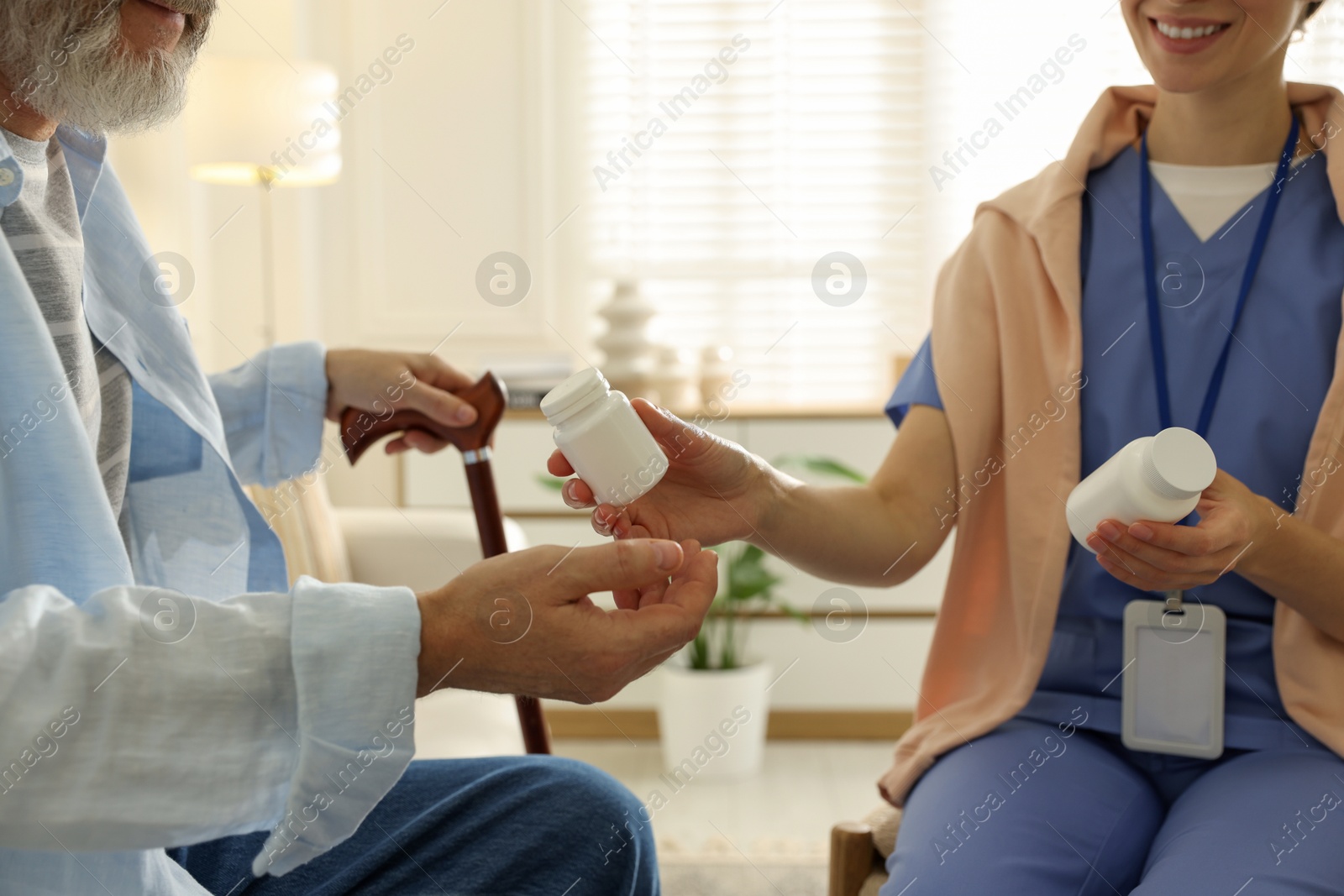 Photo of Caregiver giving pills to senior man indoors, closeup. Home health care service