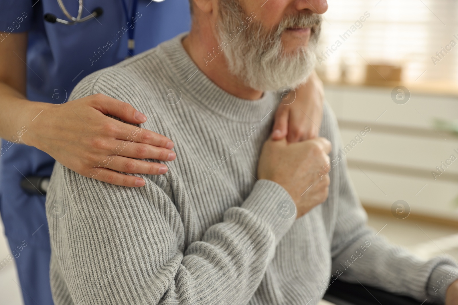 Photo of Caregiver assisting senior man in wheelchair indoors, closeup. Home health care service