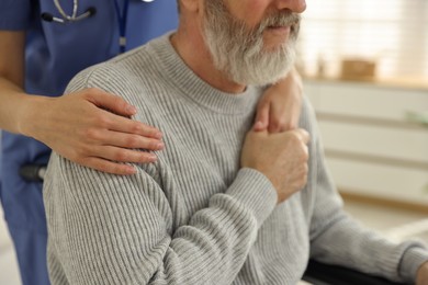 Caregiver assisting senior man in wheelchair indoors, closeup. Home health care service