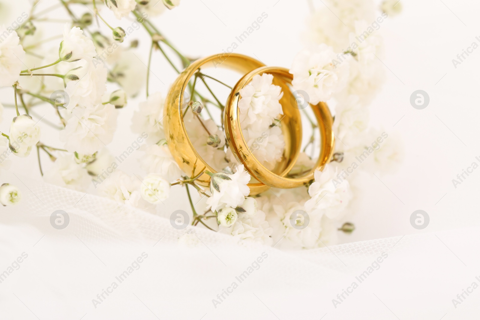 Photo of Golden wedding rings, veil and flowers on blurred background, closeup