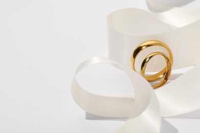 Photo of Golden wedding rings and ribbon on white background, closeup. Space for text