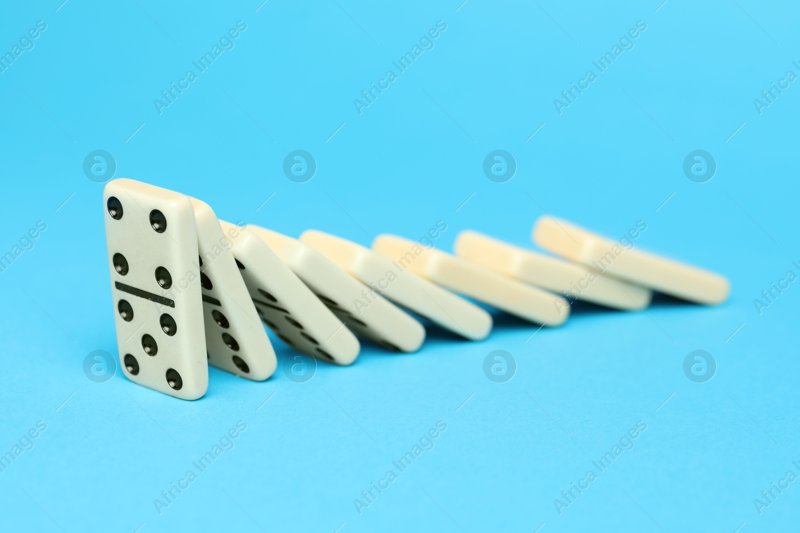 Photo of Domino effect. Tiles falling on light blue background