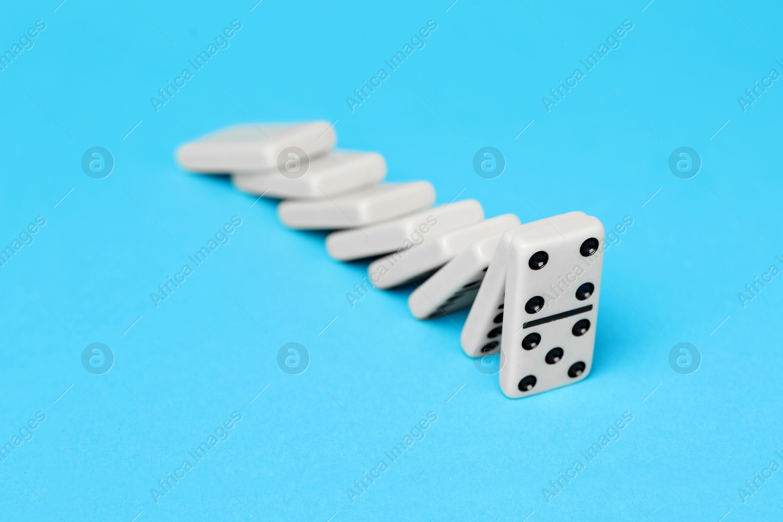 Photo of Domino effect. Tiles falling on light blue background