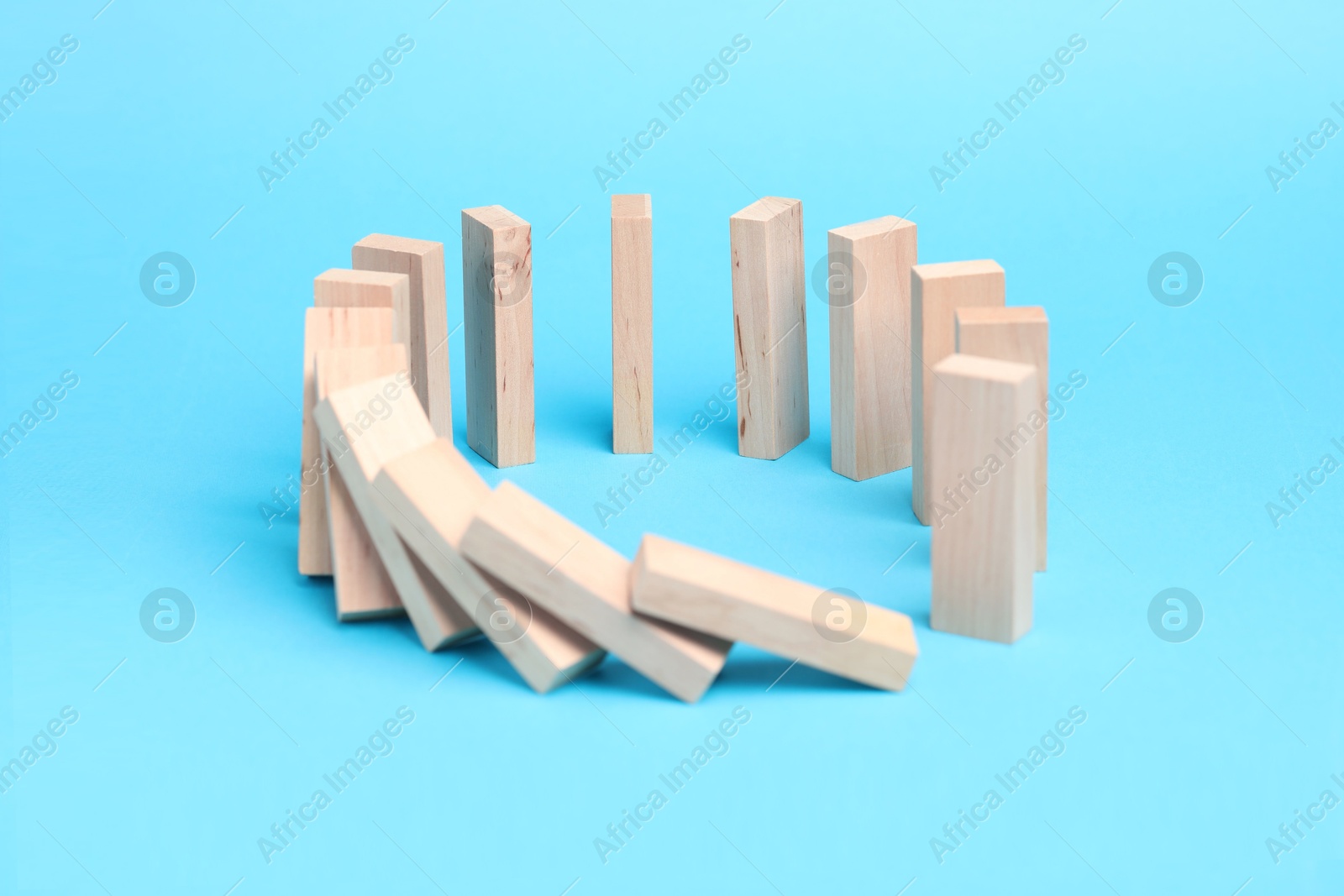 Photo of Domino effect. Wooden blocks falling on light blue background