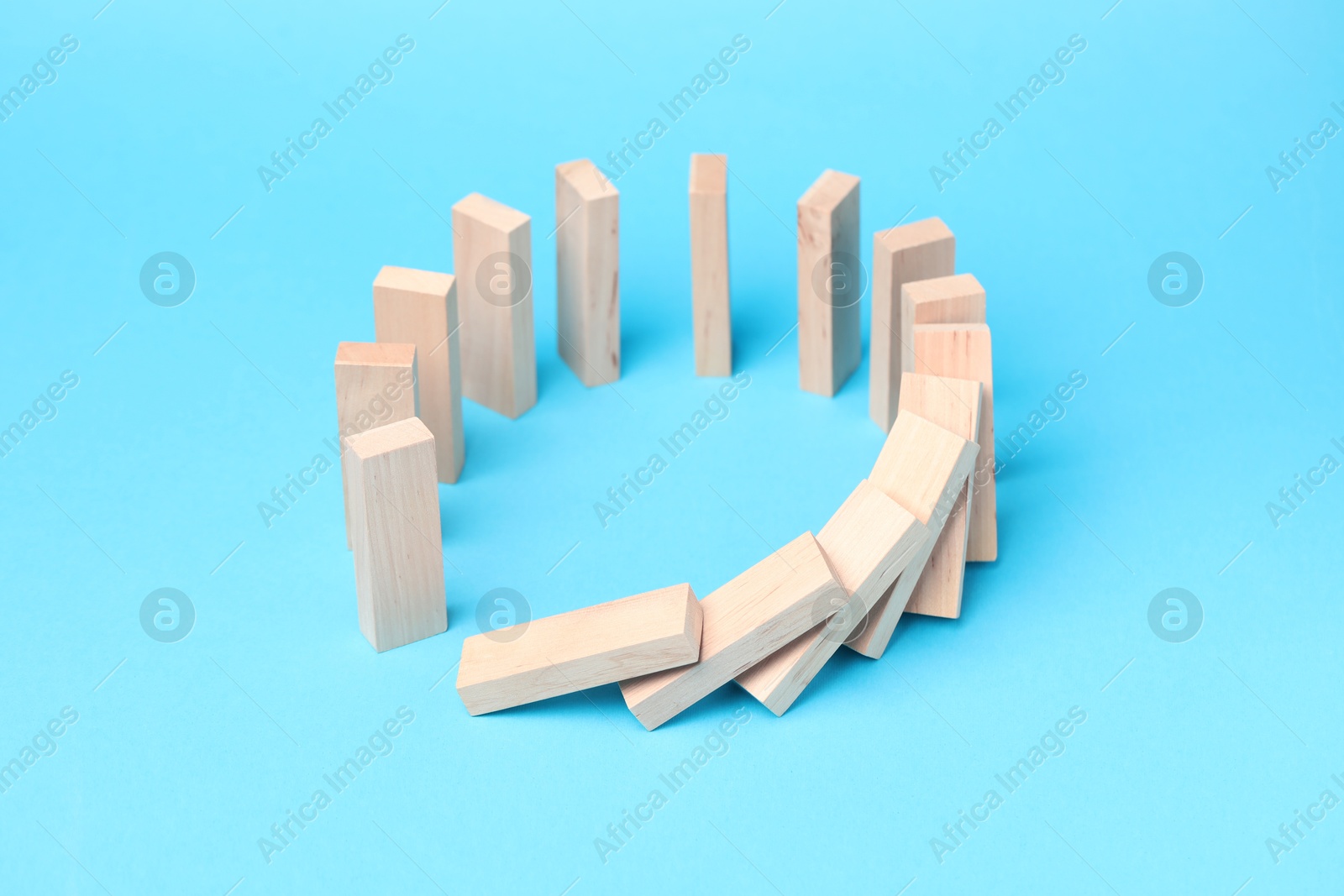 Photo of Domino effect. Wooden blocks falling on light blue background