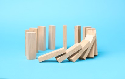 Photo of Domino effect. Wooden blocks falling on light blue background