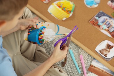 Photo of Creating vision board. Little boy cutting out picture indoors, closeup