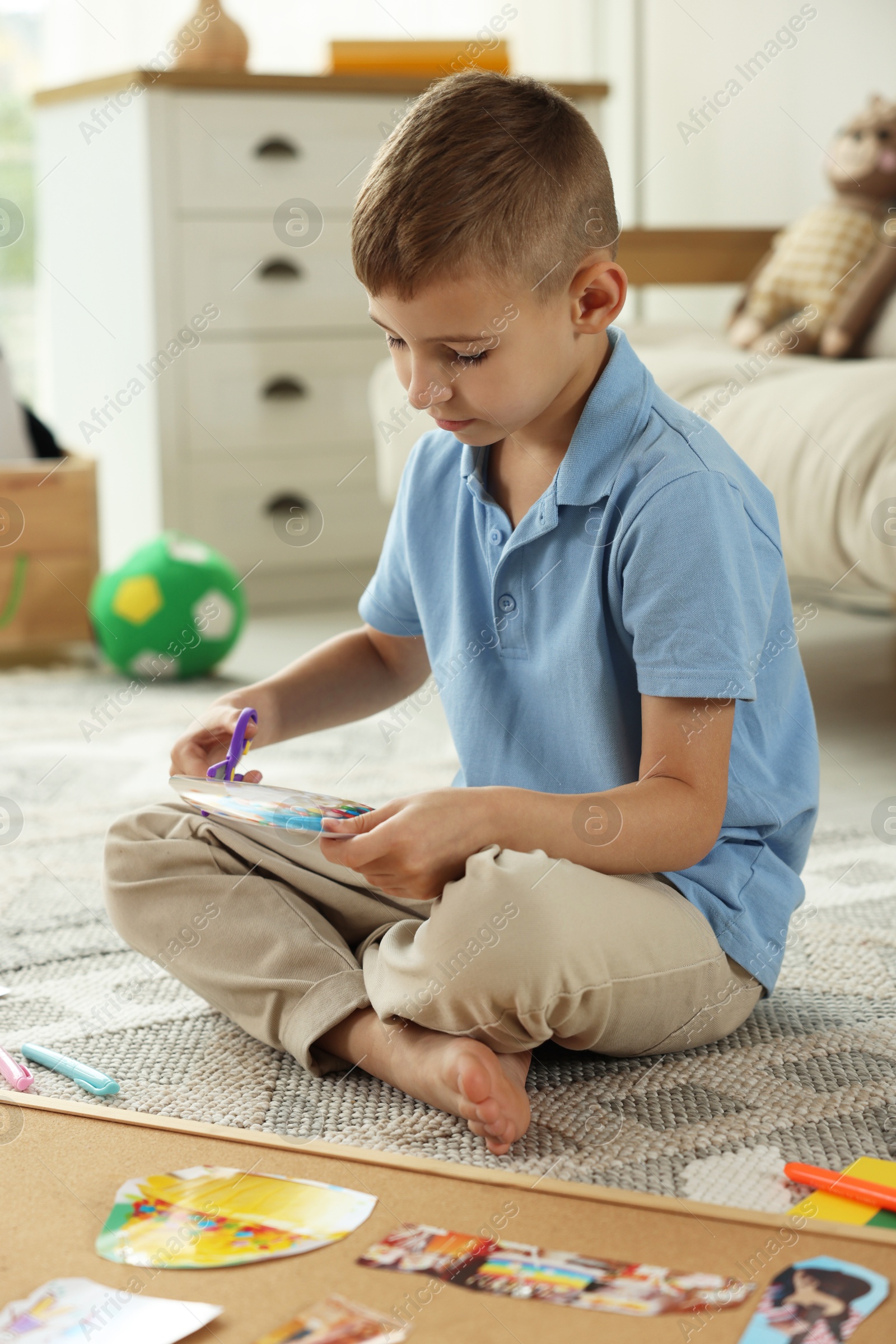 Photo of Creating vision board. Little boy cutting out picture on floor at home