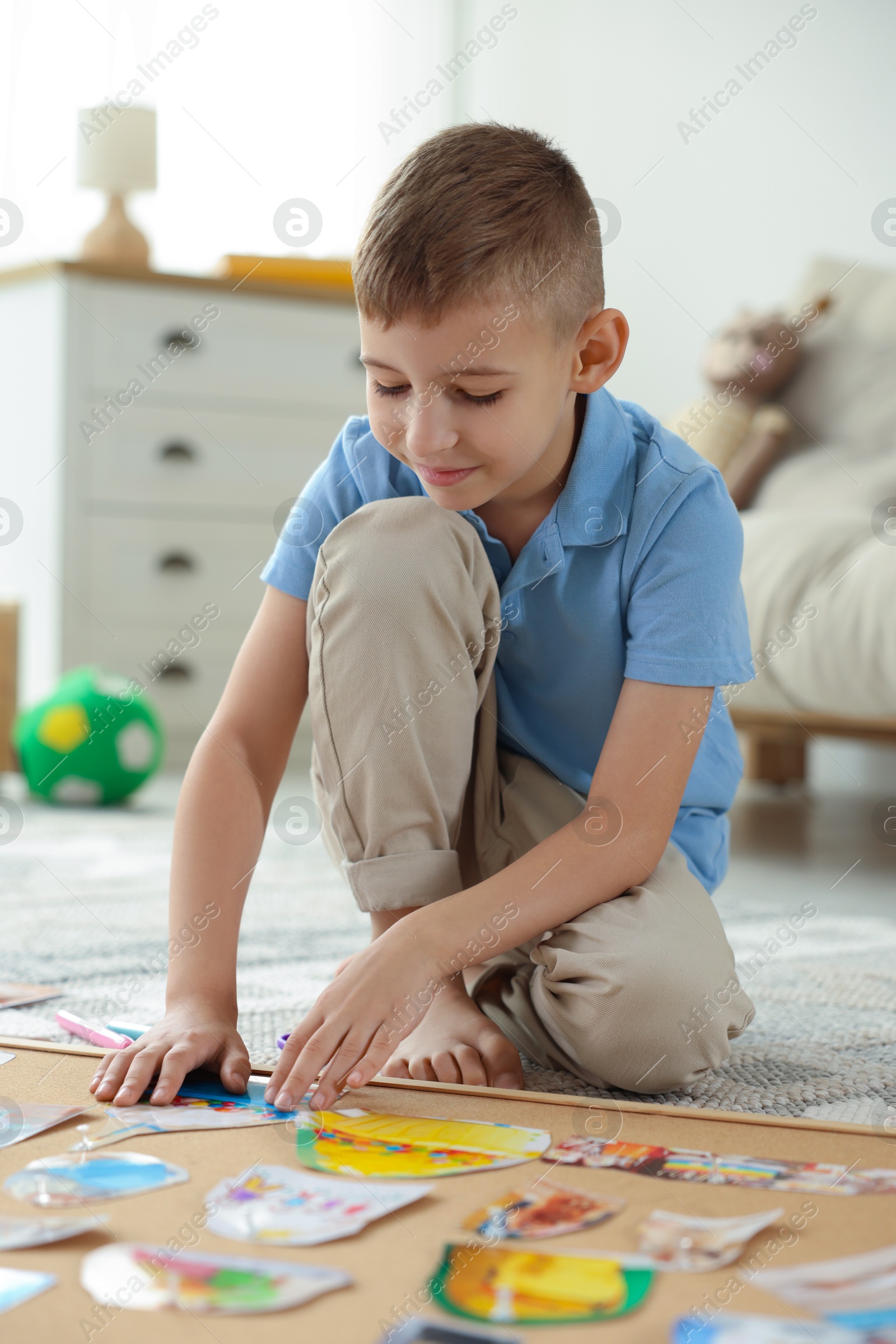 Photo of Little boy creating vision board with different pictures and other elements on floor at home