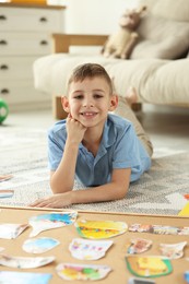 Photo of Little boy near vision board with different pictures and other elements on floor indoors