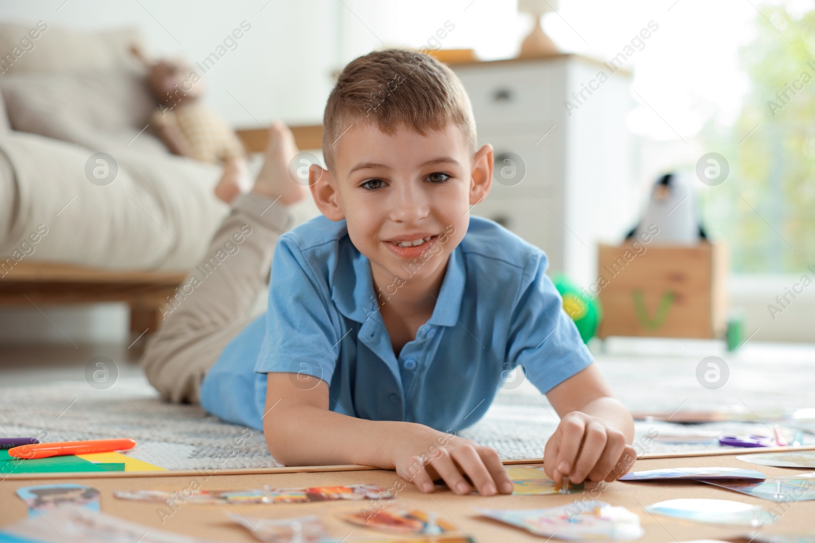 Photo of Little boy creating vision board with different pictures and other elements on floor at home