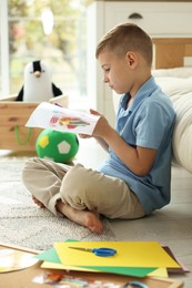 Photo of Creating vision board. Little boy cutting out picture on floor at home