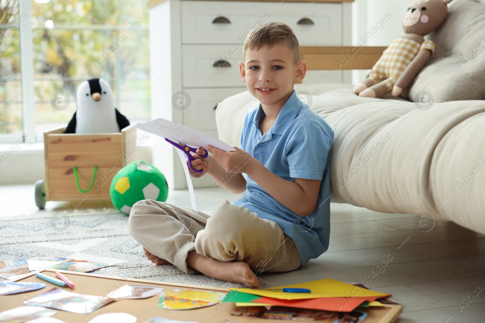 Photo of Creating vision board. Little boy cutting out picture on floor at home