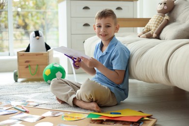 Photo of Creating vision board. Little boy cutting out picture on floor at home