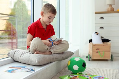 Photo of Creating vision board. Little boy cutting out picture near window indoors