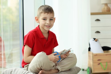 Photo of Creating vision board. Little boy cutting out picture near window indoors