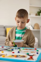 Creating vision board. Little boy cutting out picture at table indoors