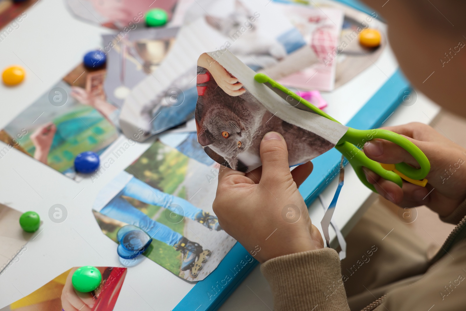 Photo of Creating vision board. Little boy cutting out picture at table indoors, closeup