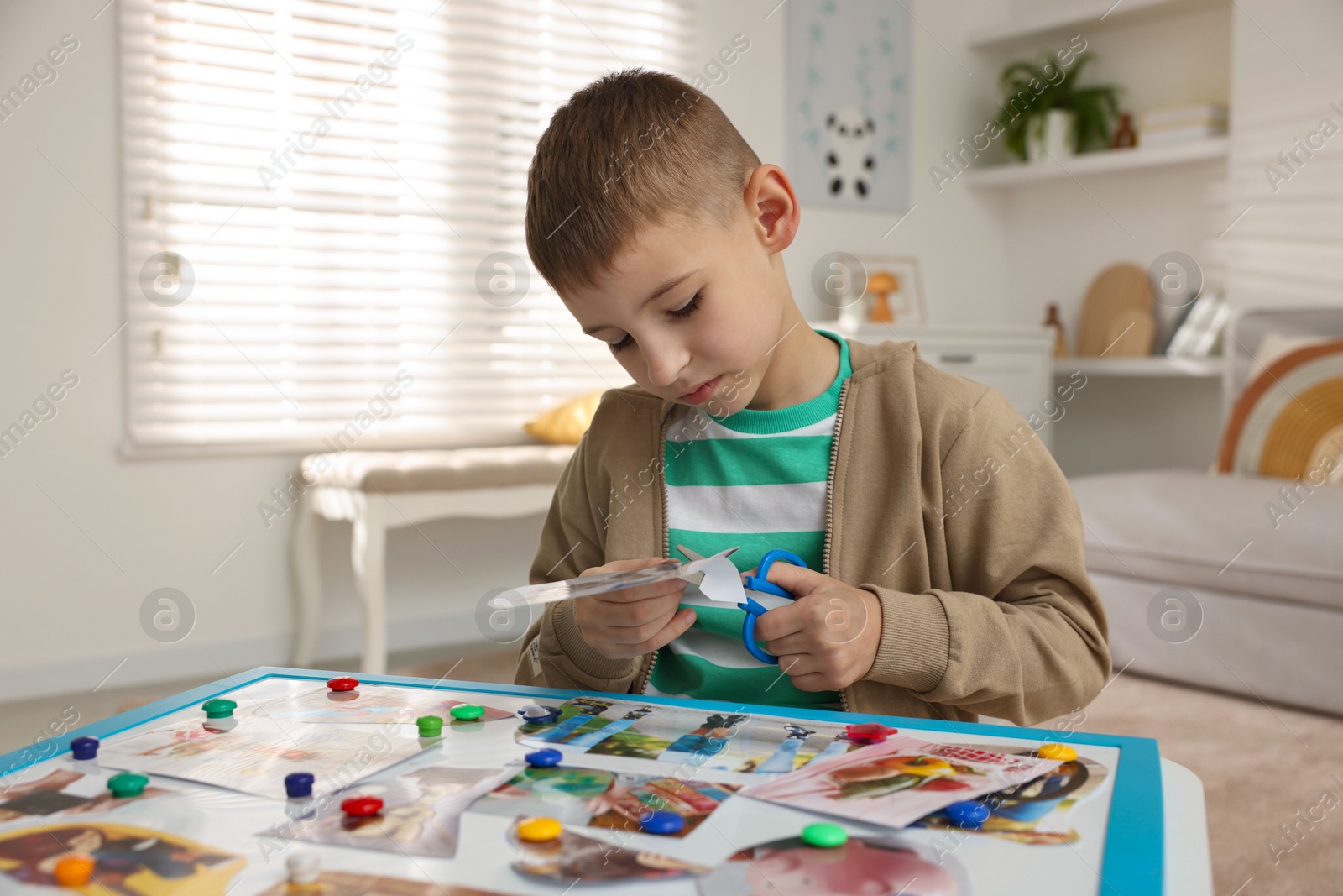 Photo of Creating vision board. Little boy cutting out picture at table indoors