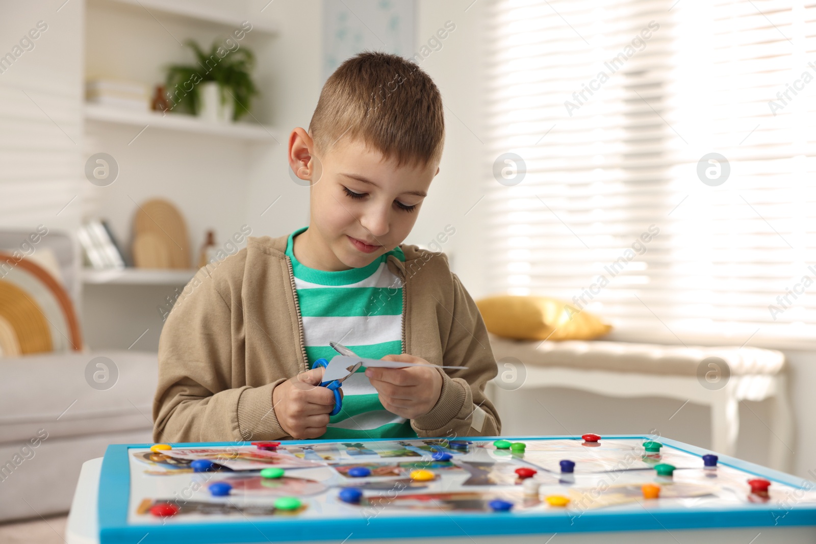 Photo of Creating vision board. Little boy cutting out picture at table indoors