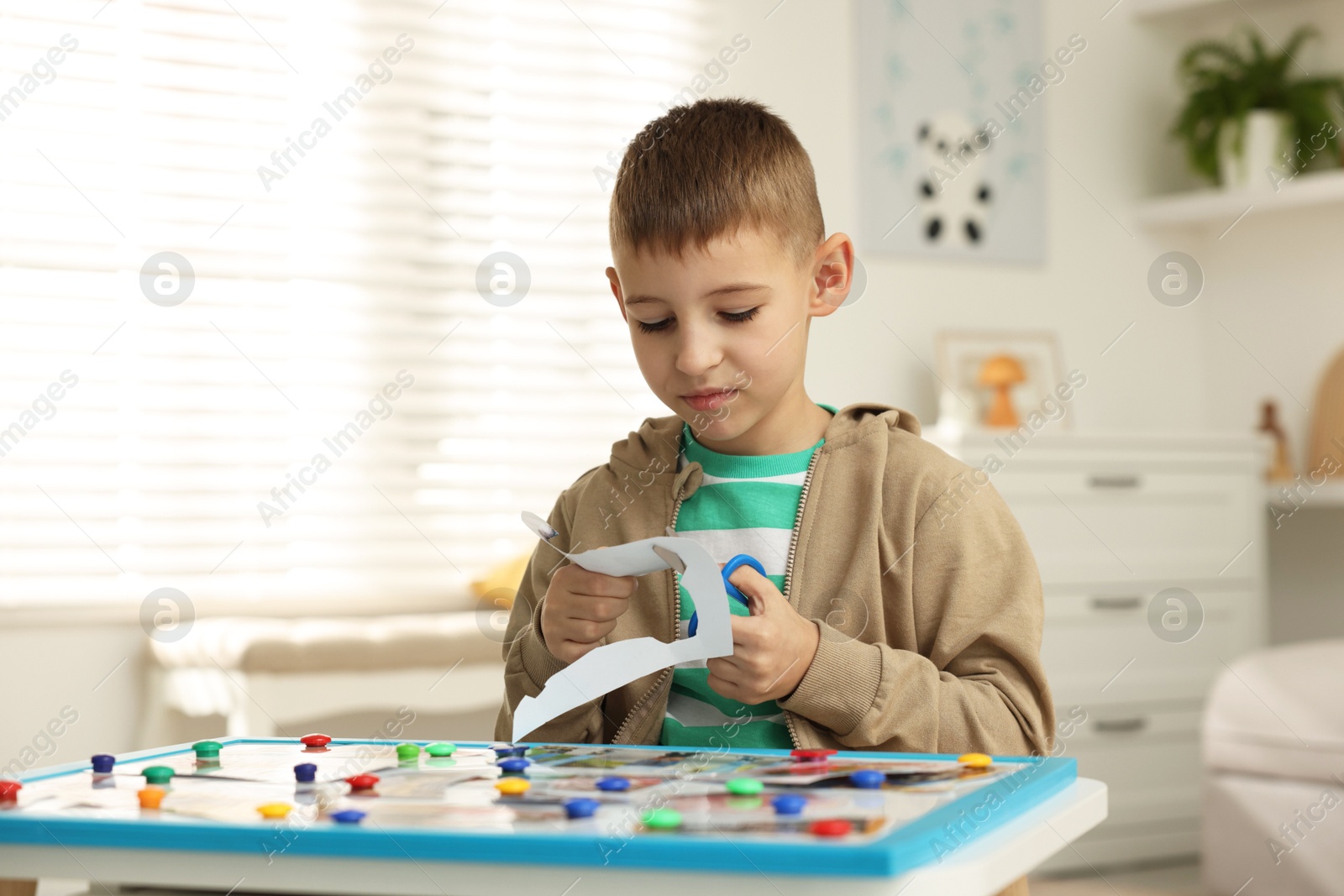 Photo of Creating vision board. Little boy cutting out picture at table indoors