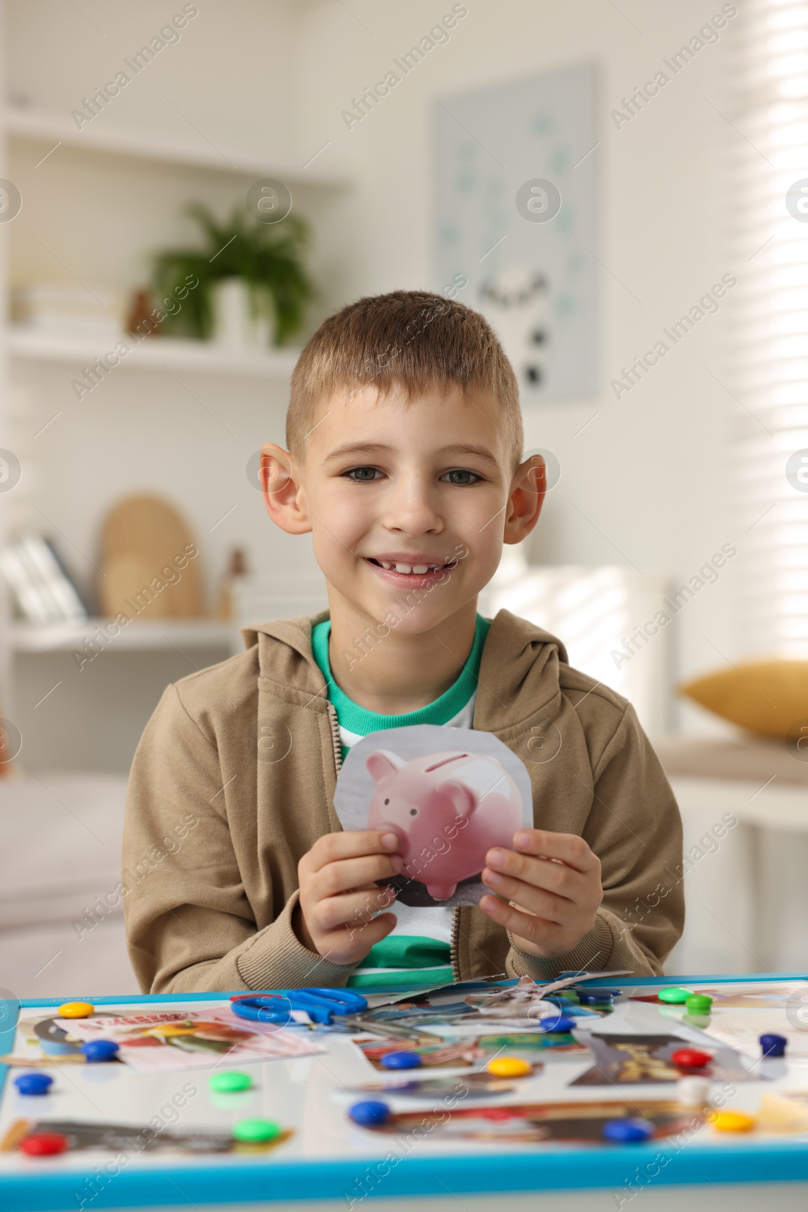 Photo of Creating vision board. Little boy with picture of piggy bank at table indoors