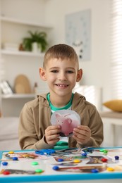 Photo of Creating vision board. Little boy with picture of piggy bank at table indoors