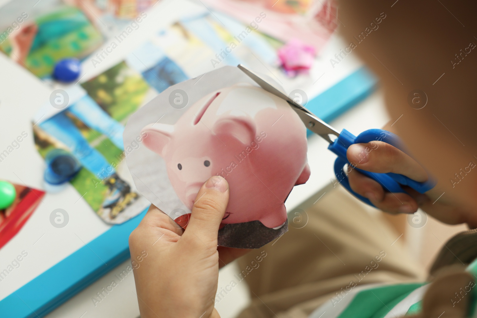 Photo of Creating vision board. Little boy cutting out picture at table indoors, closeup