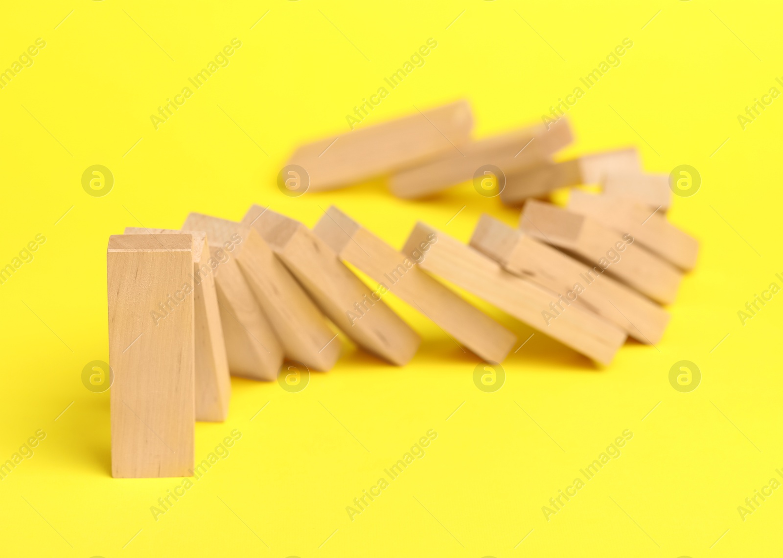 Photo of Domino effect. Wooden blocks falling on yellow background, closeup