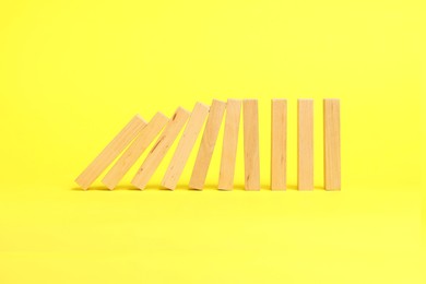 Photo of Domino effect. Wooden blocks falling on yellow background