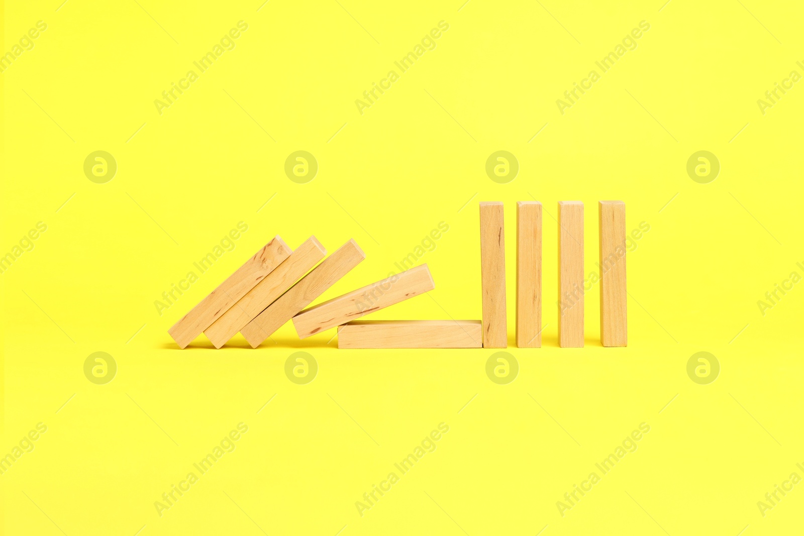 Photo of Domino effect. Wooden blocks falling on yellow background. Space for text