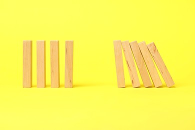 Photo of Domino effect. Wooden blocks falling on yellow background