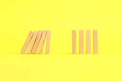 Photo of Domino effect. Wooden blocks falling on yellow background. Space for text