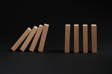 Photo of Domino effect. Wooden blocks falling on black background