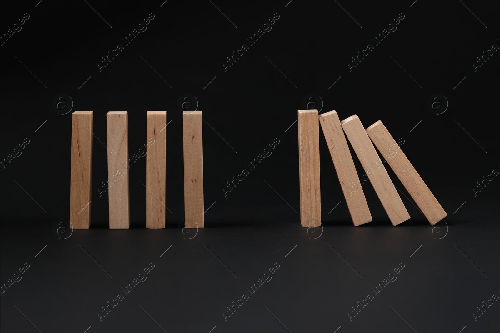 Photo of Domino effect. Wooden blocks falling on black background