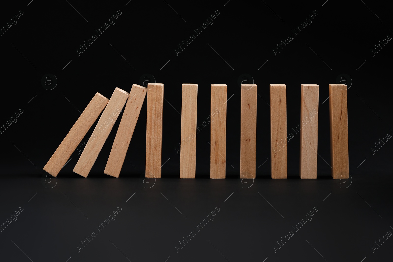 Photo of Domino effect. Wooden blocks falling on black background