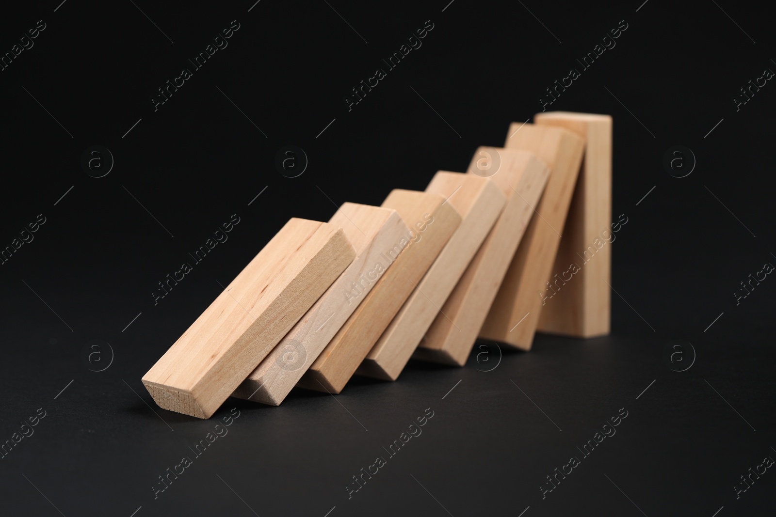 Photo of Domino effect. Wooden blocks falling on black background