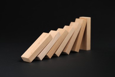 Photo of Domino effect. Wooden blocks falling on black background