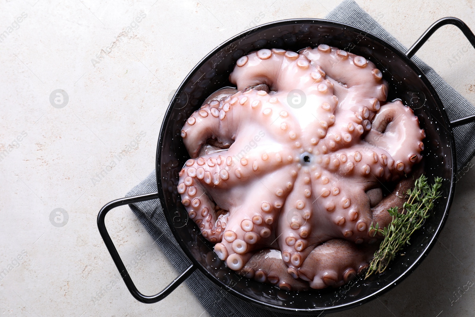 Photo of Fresh raw octopus and thyme in frying pan on grey table, top view