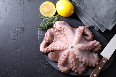 Photo of Fresh raw octopus, lemon, rosemary and knife on black table, top view. Space for text