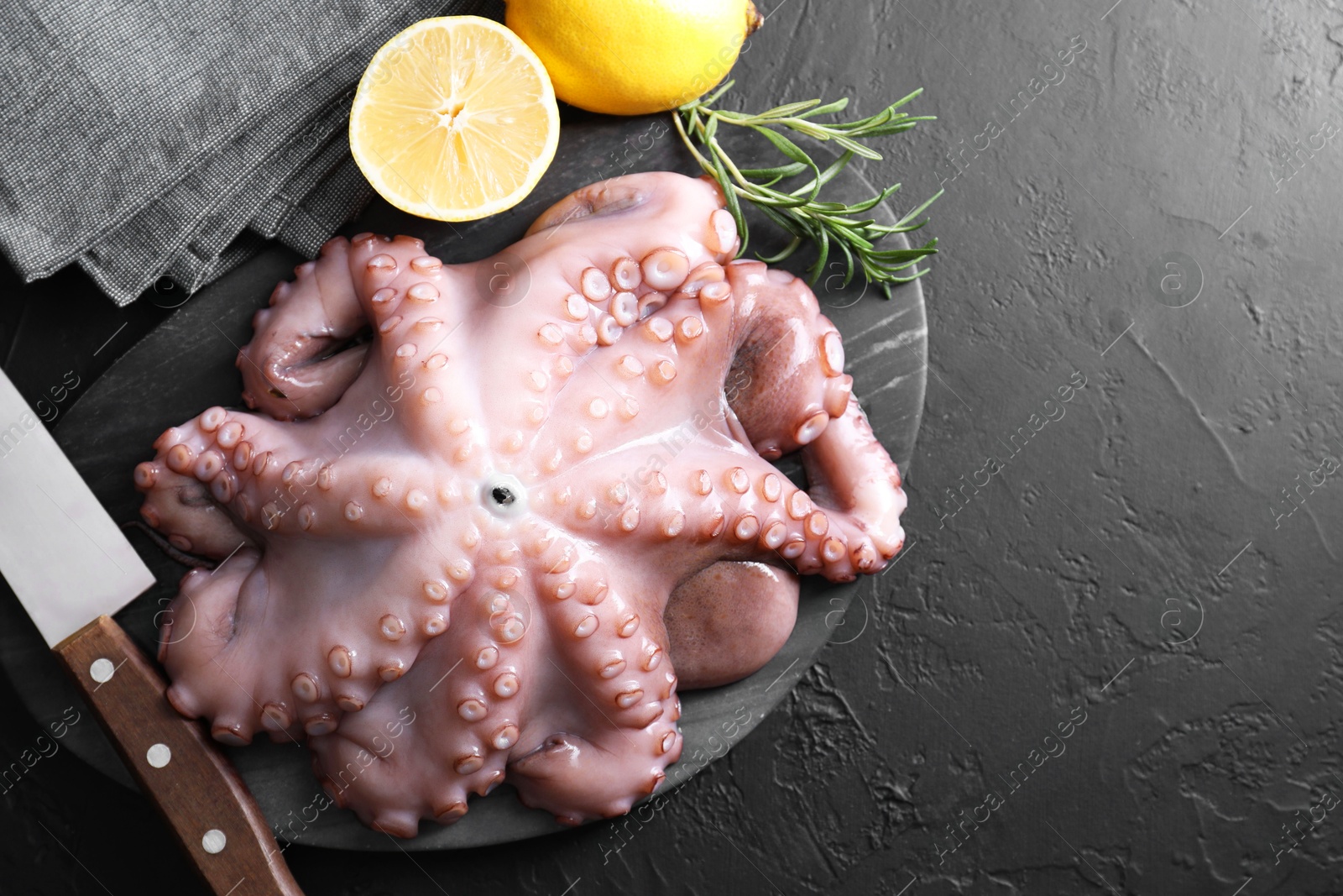 Photo of Fresh raw octopus, lemon, rosemary and knife on black table, top view. Space for text