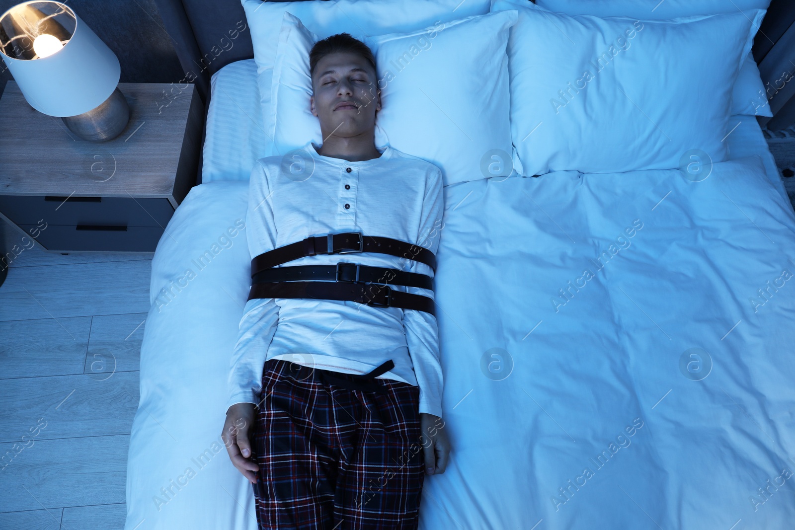 Photo of Sleepwalker fastened with belts lying on bed, above view