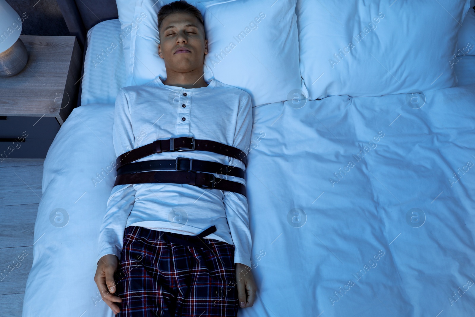 Photo of Sleepwalker fastened with belts lying on bed, above view