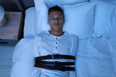 Photo of Sleepwalker fastened with belts lying on bed, top view